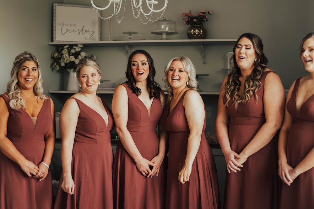 6 classy bridesmaids in brick-red, long, chiffon dresses seeing the bride for the first time.