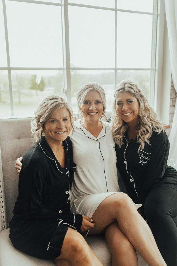 Classy bride and two bridesmaids in matching black and white pajamas sitting in front of a window at the bridal suite. 