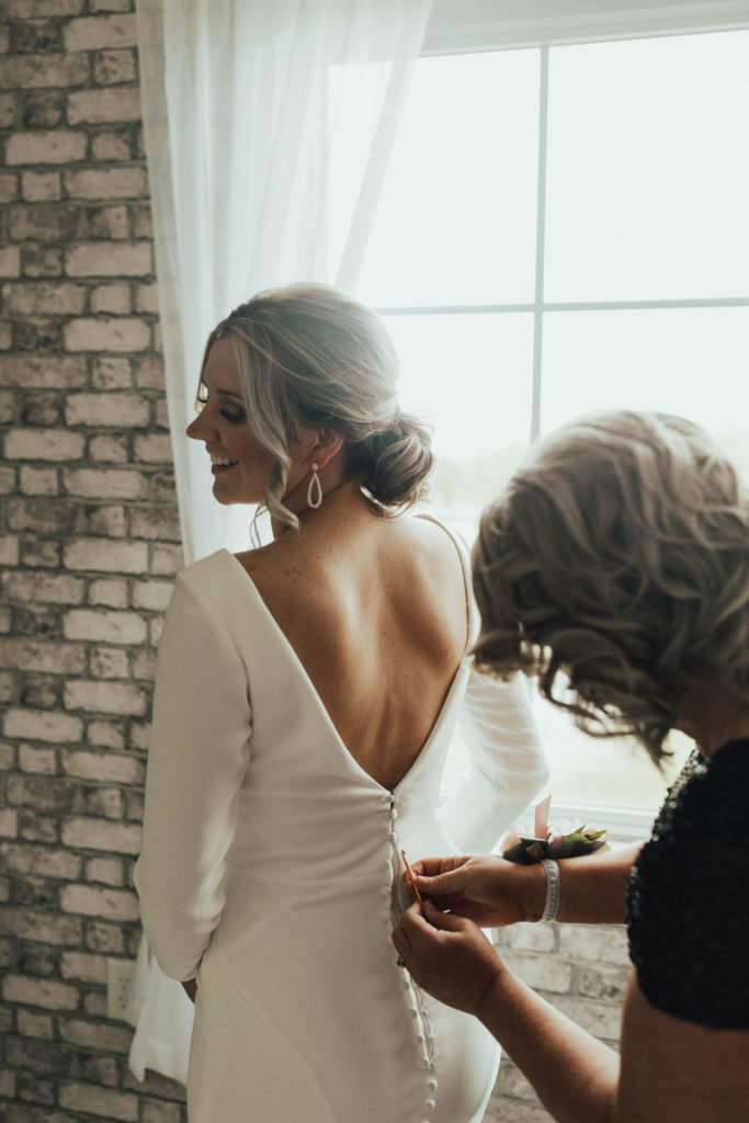 Mother of the bride zipping up the bride's elegant low back wedding dress.