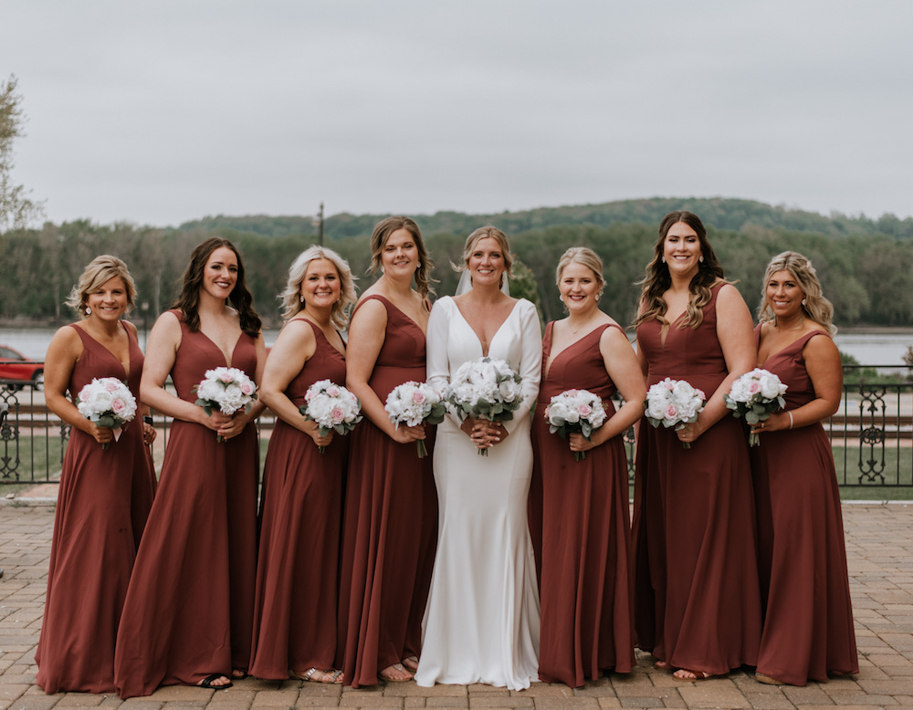 Bride and her bridesmaids wearing brick-red, long chiffon bridesmaid dresses and holding classy white bouquets