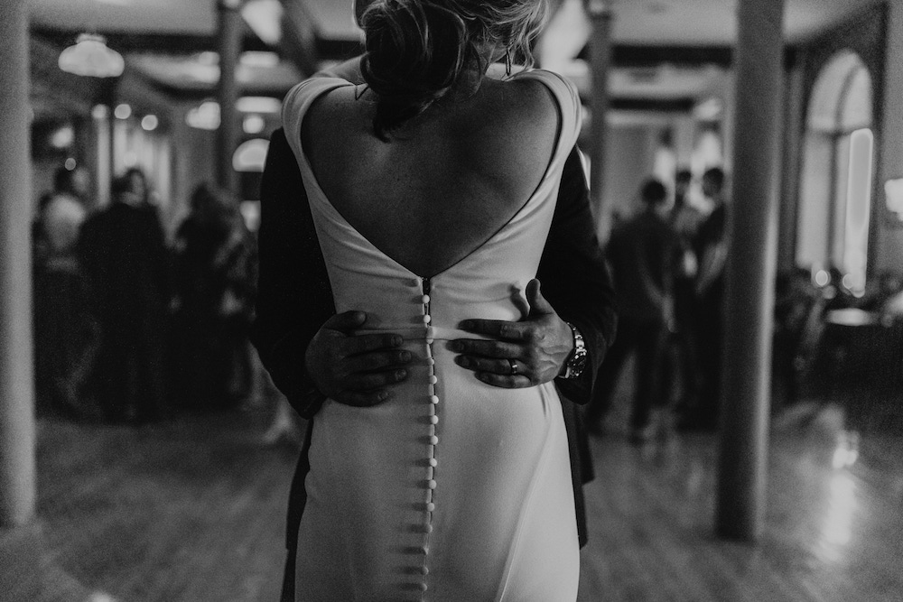 Bride wearing a fitted wedding dress with buttons down the back and groom having their first dance