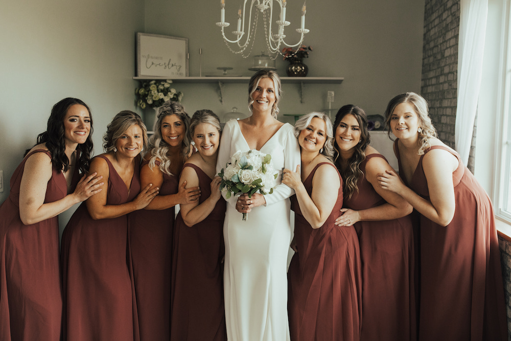 Bride and her 7 bridesmaids wearing brick-red, long, chiffon bridesmaid dresses. 