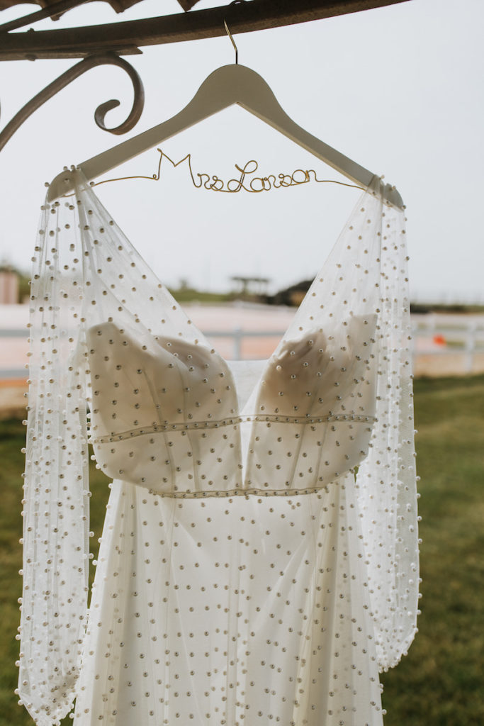 Sheer wedding dress with pearls on a custom wooden hanger. 