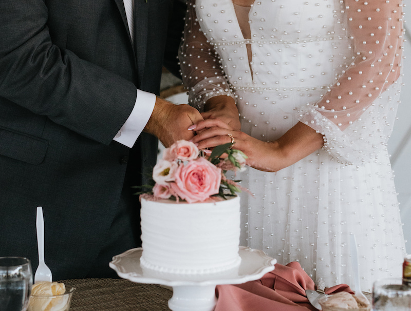 Bride and groom cutting their one tier buttercream cake with white frosting and pink roses. 