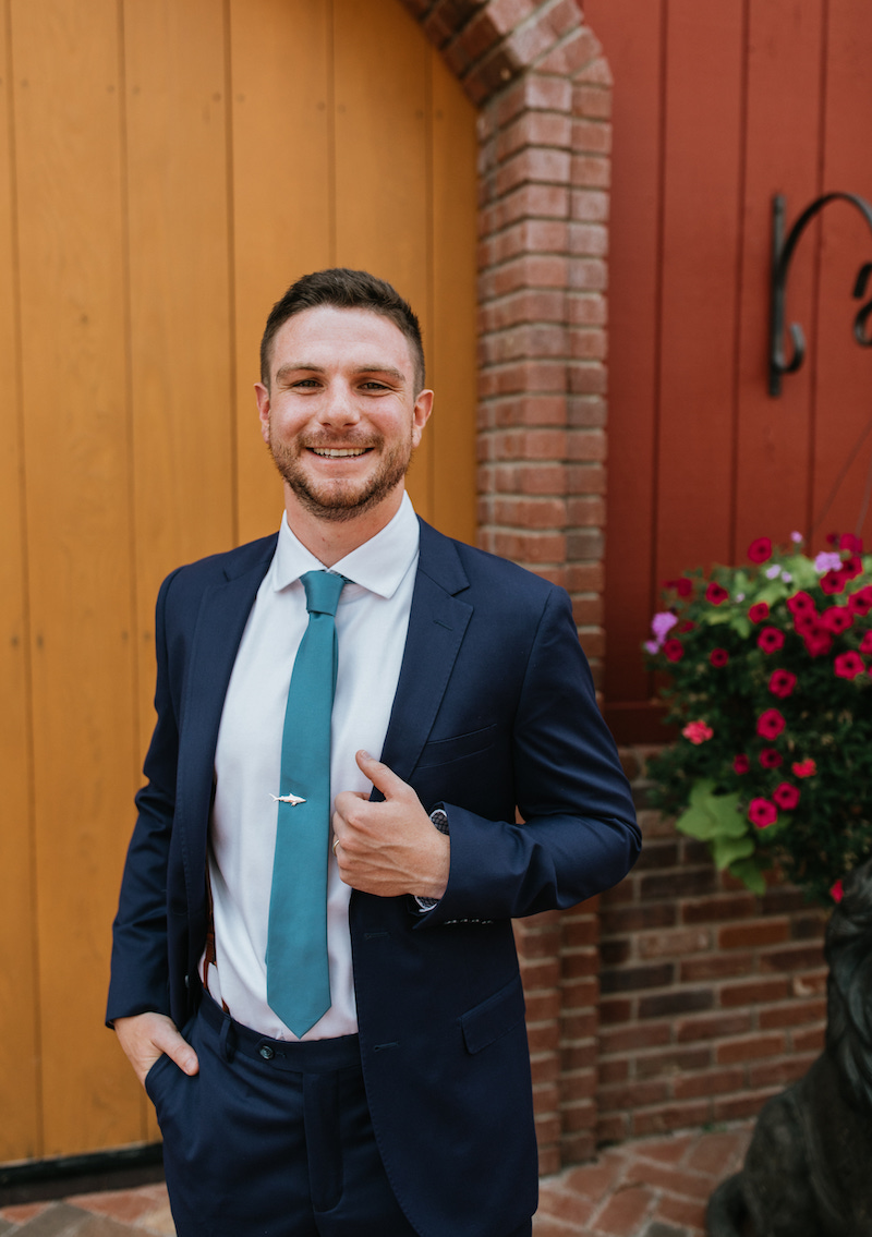 Groom in a blue suit with a teal tie and intentional shark tie pin. 