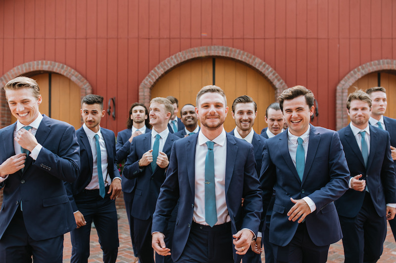 Groom and groomsmen wearing blue suits and teal ties walking towards the camera. 