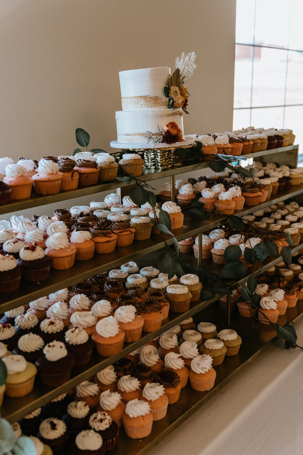 Fall wedding dessert table with a white buttercream cake and variety of flavored cupcakes. 