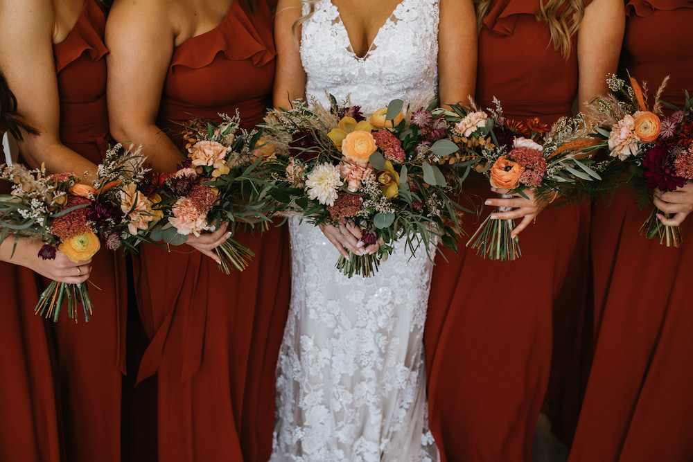Bride and bridesmaids wearing burnt orange dresses holding matching fall colored bouquets. 