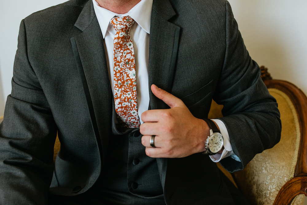 Groom wearing a grey suit and burnt orange floral tie for his fall wedding in Iowa. 